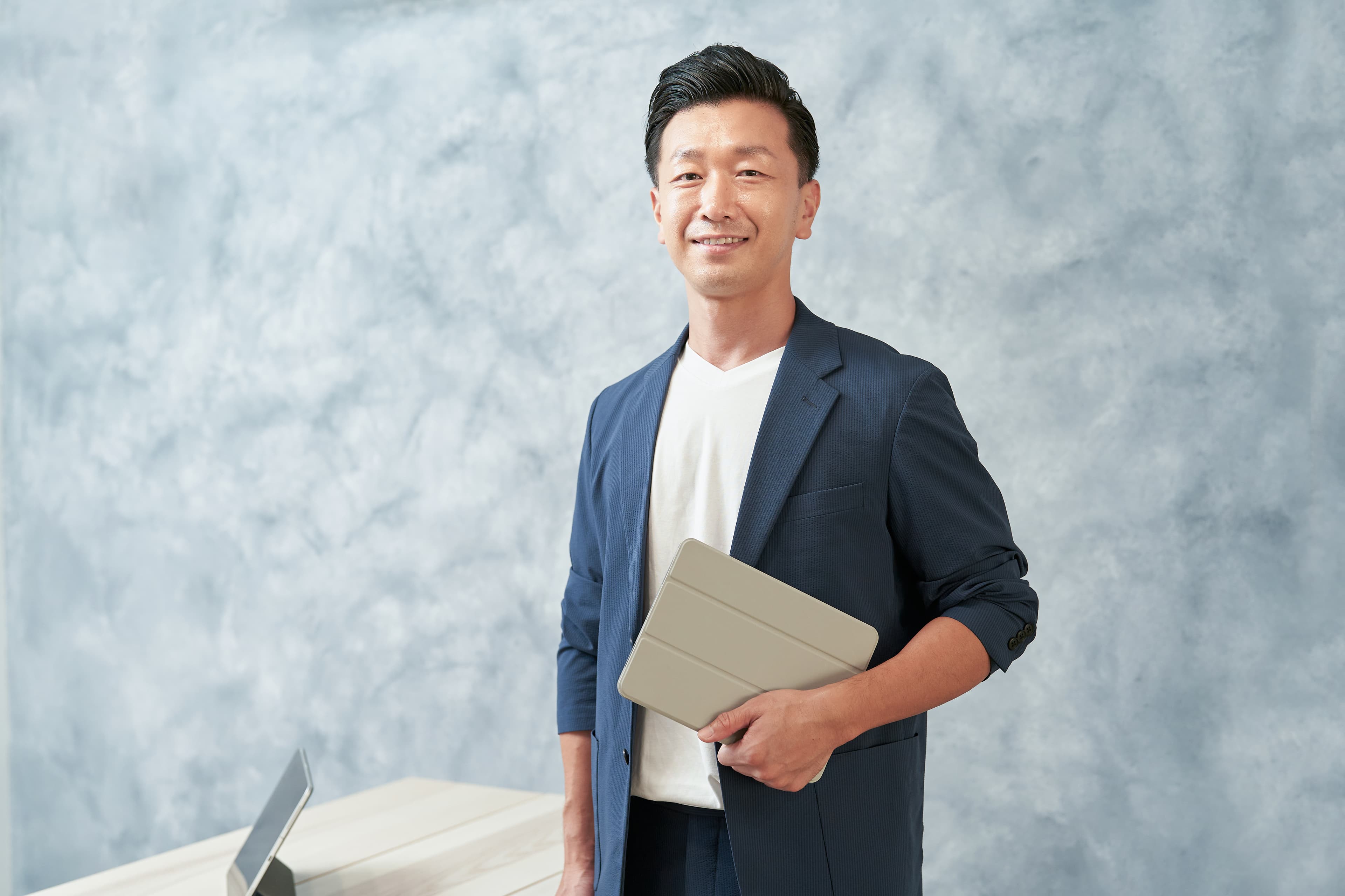 タブレットを手に微笑む紺ジャケットの男性ビジネスパーソン。沖縄での即戦力IT人材採用のイメージ